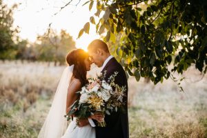 bride and groom in a field at sunset holding a bridal bouquet of dahlias, roses eucylyptus